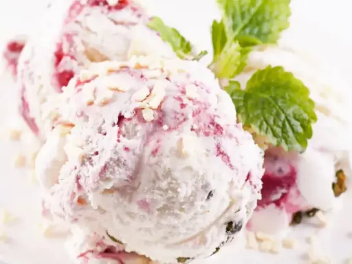 Pyszne lody z mascarpone z malinową nutą i chrupiącymi kawałkami białej czekolady, ozdobione listkiem mięty.