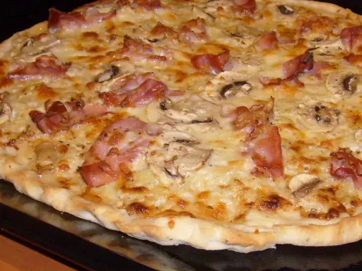 Pyszna pizza carbonara z chrupiącym boczkiem, pieczarkami i ciągnącym się serem. Idealna na szybki obiad.