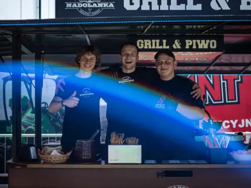 Trzech uśmiechniętych mężczyzn za ladą cateringową z napisem "Grill & Piwo".
