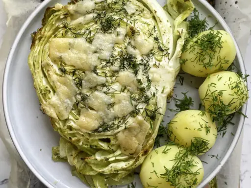 Pieczona młoda kapusta z serem i koperkiem, podana z młodymi ziemniakami. Idealny pomysł, co zrobić z młodej kapusty na obiad.