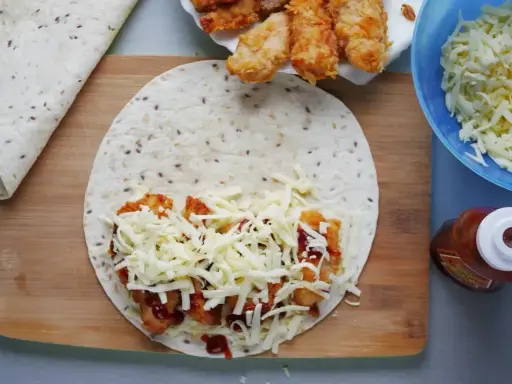 Tortilla z kurczakiem, serem i sosem na desce. Obok miska z serem i butelka ketchupu.