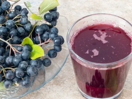 Świeża aronia na talerzu i szklanka soku. Idealne do przygotowania przetworów, np. jak mrozić aronię na zimę.