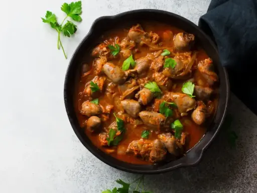 Serca drobiowe w gęstym, aromatycznym sosie, udekorowane świeżą natką pietruszki, podane w żeliwnej patelni.