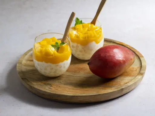 Pyszny deser z tapioki i mango, idealny sposób, by wykorzystać mrożone mango. Podany w szklankach z drewnianymi łyżeczkami.