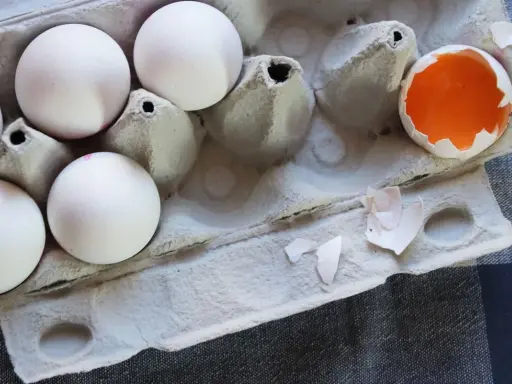 Białe jajka w wytłoczce, jedno rozbite z widocznym żółtkiem. Zastanawiasz się, czy jajka można mrozić?
