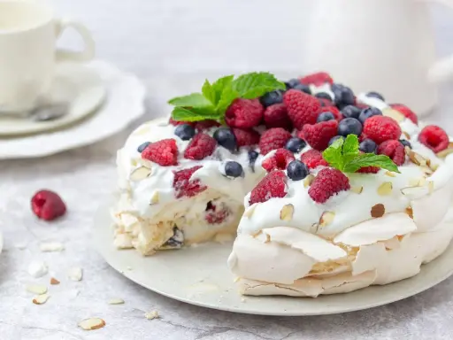 Beza Pavlova która zawsze wychodzi, udekorowana bitą śmietaną, malinami, borówkami i listkami mięty. Idealna na deser.