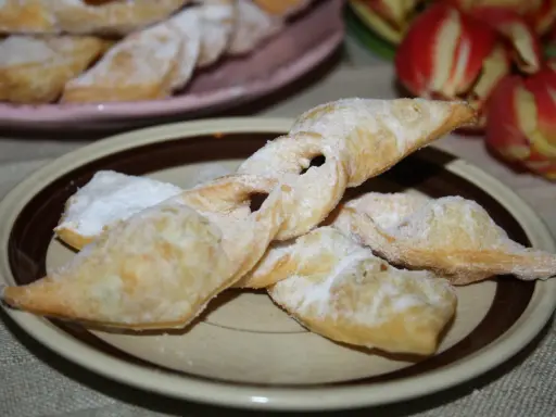 Chrupiące faworki, przepis babci, posypane cukrem pudrem, na talerzu obok tulipanów.