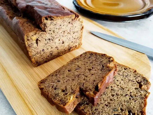 Wilgotny chleb bananowy pokrojony na desce, obok nóż i talerz.