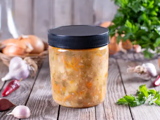 Słoik z domową zupą warzywną, obok cebula, czosnek i chili. Dowiedz się, jakich zup nie można mrozić.