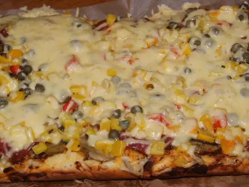 Pyszna pizza na grubym cieście z warzywami i roztopionym serem.