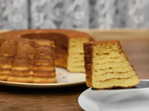 Kawałek sękacza z widocznymi warstwami na talerzyku, w tle cały sękacz.