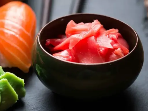 Miseczka z marynowanym imbirem do sushi, obok kawałka sushi z łososiem i wasabi.