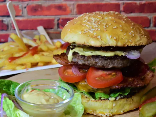 Soczysty burger z wołowiny, bekonem, warzywami i frytkami w tle.