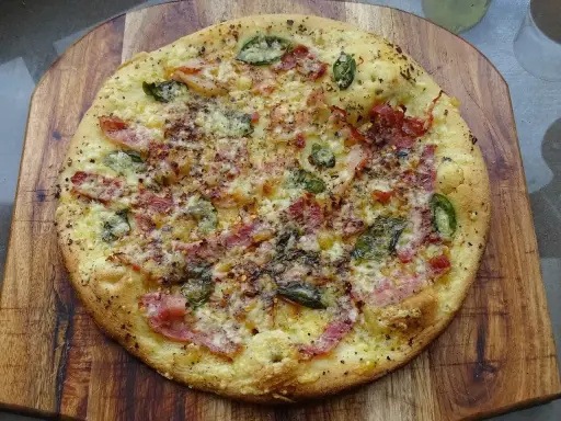 Pyszna pizza bianca z szynką, serem i zielonymi dodatkami, posypana przyprawami, na drewnianej desce.
