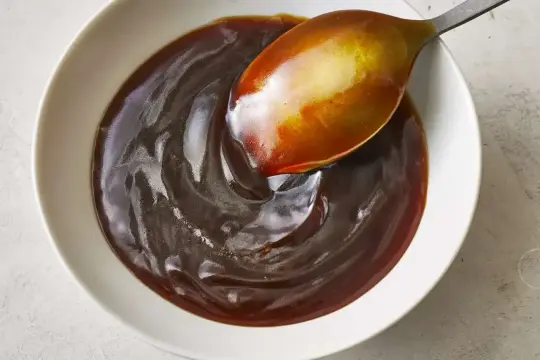 Gęsty, błyszczący sos teriyaki w białej miseczce, nabierany łyżką. Idealny do marynowania mięsa.