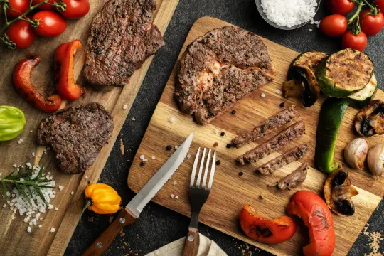 Pyszny stek z grilla, pokrojony w plastry, podany z grillowanymi warzywami i pomidorkami.