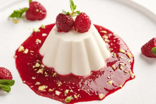 Panna cotta, pyszny włoski deser, podana z malinowym sosem, malinami i pistacjami.