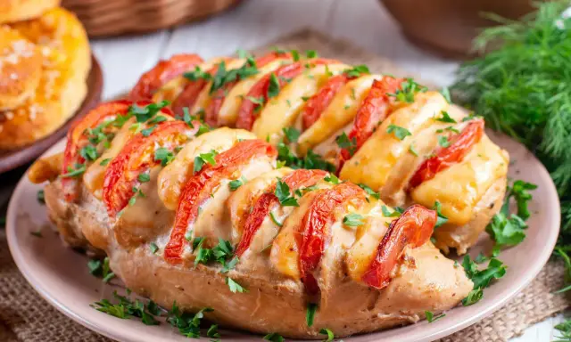 Pyszny pomysł, co zrobić z fileta z kurczaka na obiad: pieczony filet z kurczaka z pomidorami i serem, posypany natką pietruszki.