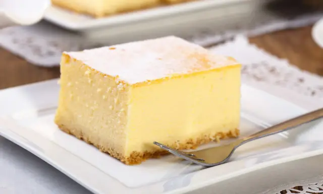 Pyszny sernik z wiaderka, idealny do pieczenia w temperaturze 170°C. Pokrojony na kwadratowe porcje, posypany cukrem pudrem, czeka na widelczyk.