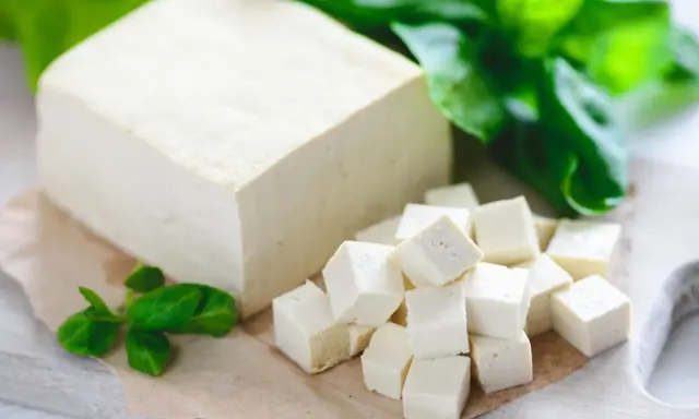 Kostka tofu i pokrojone w kostkę tofu na desce, ozdobione zielonymi liśćmi.