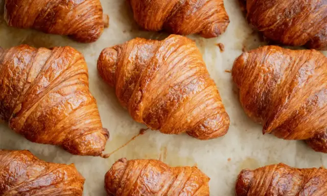 Złociste, chrupiące rogaliki ułożone na papierze do pieczenia. Idealne na śniadanie, choć warto pamiętać o ich kaloryczności – croissant kcal.