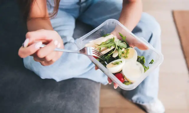 Kobieta z widelcem w dłoni je sałatkę z kurczakiem i jajkiem z pudełka. Zastanawiasz się, jaki catering dietetyczny wybrać?
