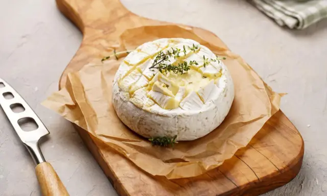 Pyszny camembert z grilla, zapieczony z ziołami, na drewnianej desce. Idealny do maczania.