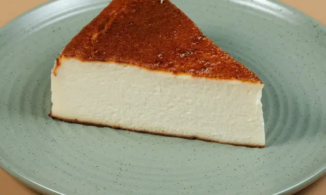 Pyszny kawałek sernika pieczonego bez spodu, z lekko przypieczoną górą, na zielonym talerzu.