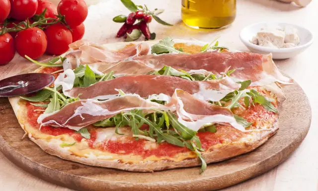 Pyszna pizza prosciutto z rukolą, pomidorkami i oliwą. Idealna na włoską ucztę.