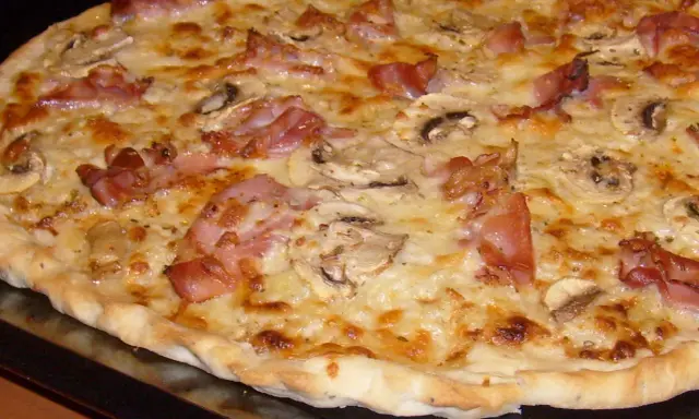 Pyszna pizza carbonara z chrupiącym boczkiem, pieczarkami i ciągnącym się serem. Idealna na szybki obiad.