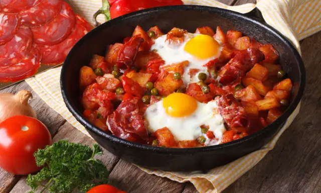 Pyszne danie z jajek na obiad: ziemniaki, chorizo, papryka i groszek zapiekane w patelni.
