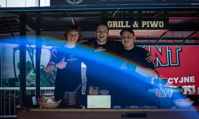 Trzech uśmiechniętych mężczyzn za ladą cateringową z napisem "Grill & Piwo".
