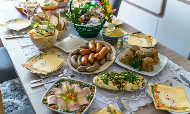 Obficie zastawiony stół z potrawami wielkanocnymi: kiełbasy, galareta, sałatki, chleb. Lista potraw wielkanocnych jest długa!