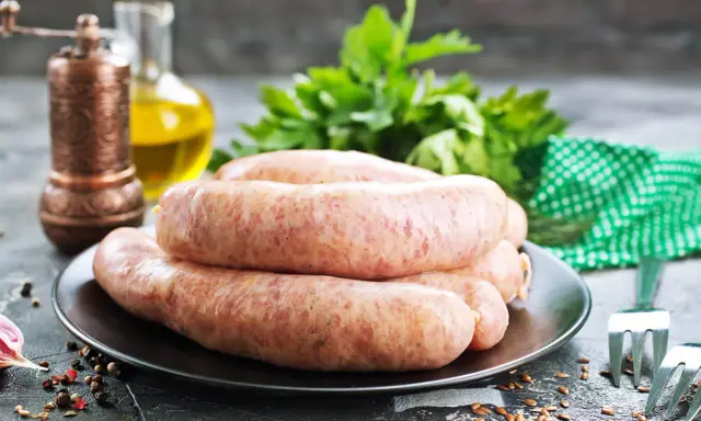 Świeża kiełbasa na talerzu, obok przyprawy i ziół. Zastanawiasz się, jak długo można mrozić kiełbasę?