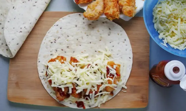 Tortilla z kurczakiem, serem i sosem na desce. Obok miska z serem i butelka ketchupu.