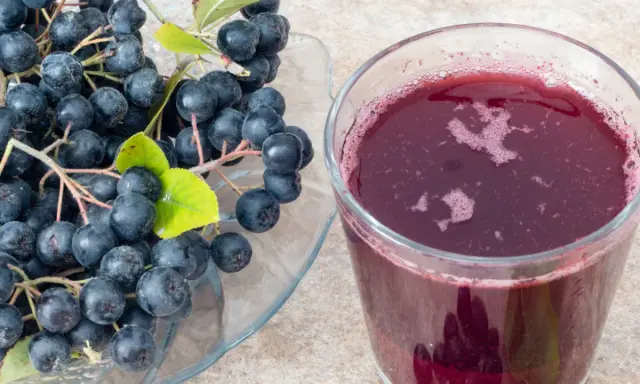 Świeża aronia na talerzu i szklanka soku. Idealne do przygotowania przetworów, np. jak mrozić aronię na zimę.