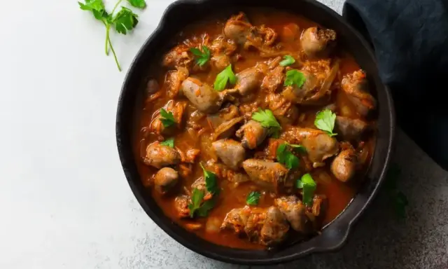 Serca drobiowe w gęstym, aromatycznym sosie, udekorowane świeżą natką pietruszki, podane w żeliwnej patelni.