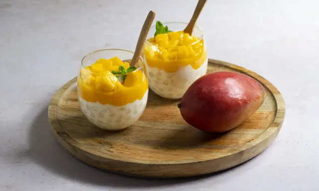 Pyszny deser z tapioki i mango, idealny sposób, by wykorzystać mrożone mango. Podany w szklankach z drewnianymi łyżeczkami.