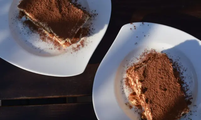 Dwa kawałki tiramisu posypane kakao na białych talerzach. Idealne do mocnej kawy, która podkreśli smak.
