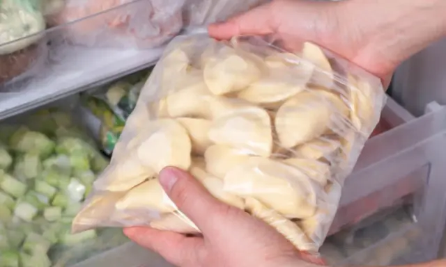 Ręce wkładają do zamrażarki worek z pierogami. To prosty sposób, jak mrozić pierogi, by cieszyć się nimi później.