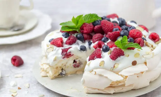 Beza Pavlova która zawsze wychodzi, udekorowana bitą śmietaną, malinami, borówkami i listkami mięty. Idealna na deser.