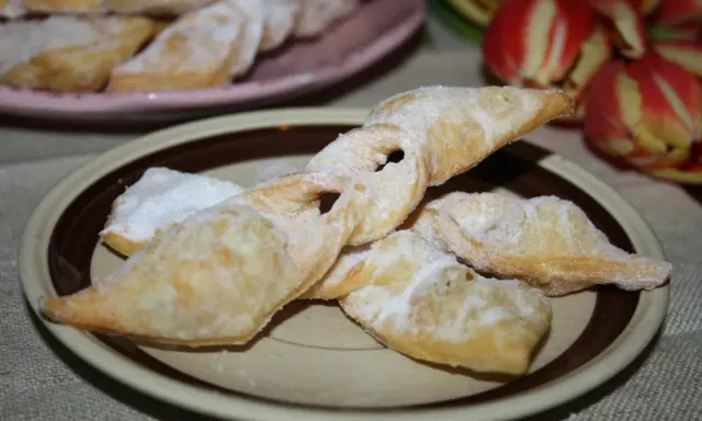 Chrupiące faworki, przepis babci, posypane cukrem pudrem, na talerzu obok tulipanów.