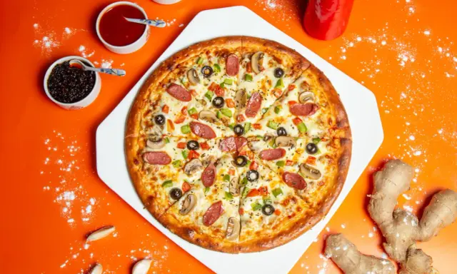 Chrupiąca pizza z pieczarkami, salami i papryką na pomarańczowym tle.