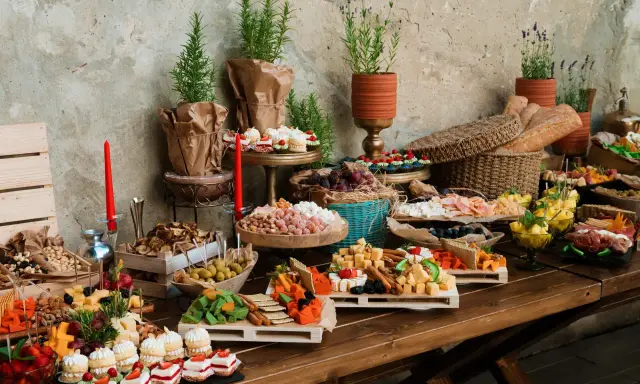 Bogaty stół z serami, owocami, ciastkami i pieczywem. Idealny na przyjęcie, zastanawiasz się, ile kosztuje catering na 15 osób?