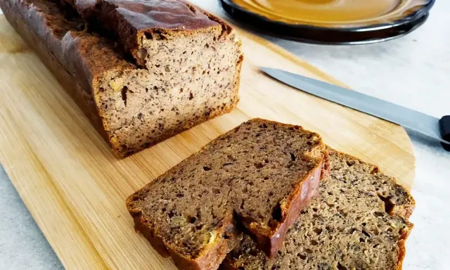 Wilgotny chleb bananowy pokrojony na desce, obok nóż i talerz.
