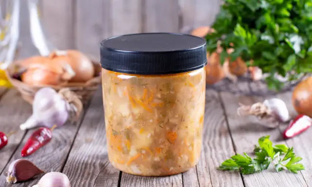 Słoik z domową zupą warzywną, obok cebula, czosnek i chili. Dowiedz się, jakich zup nie można mrozić.