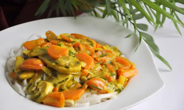 Zdrowy obiad: makaron ryżowy z warzywami w sosie curry. Kolorowe marchewki i inne warzywa tworzą apetyczną kompozycję.