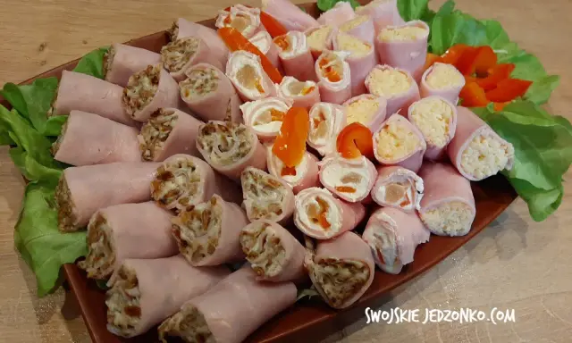Talerz z roladkami z szynki z różnymi nadzieniami, ozdobiony sałatą i papryką.