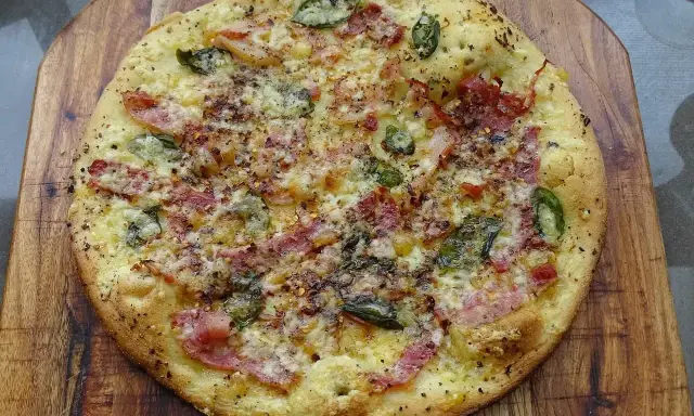 Pyszna pizza bianca z szynką, serem i zielonymi dodatkami, posypana przyprawami, na drewnianej desce.