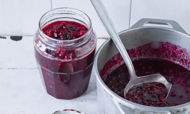 Słoik z konfiturą żurawinową i chochla w garnku z konfiturą.